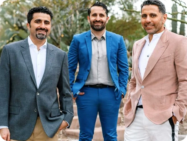 A group portrait of three men, including all Dr. Torabi in a bright blue suit, standing outdoors in a desert landscape with cacti in the background. They are dressed in professional blazers and slacks, smiling at the camera.