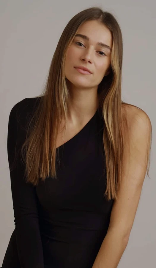 A portrait of a woman with long, straight hair wearing a black one-shoulder top, looking directly at the camera against a neutral studio background.