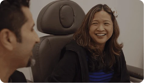 A candid moment during a consultation where a female patient with a flower in her hair laughs joyfully. Dr. Torabi's profile is partially visible in the foreground as they converse.