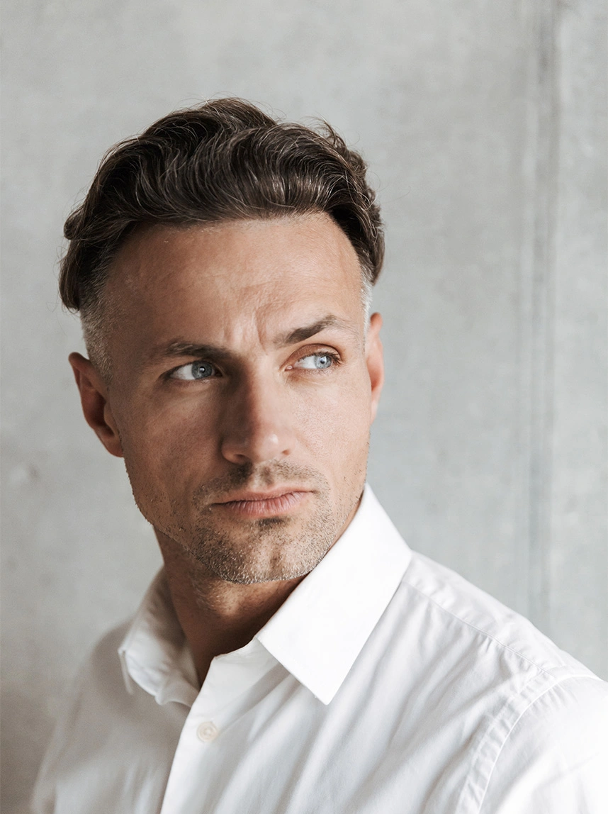 A close-up portrait of a man with short, styled brown hair and blue eyes, wearing a crisp white button-down shirt, looking off-camera with a clear and healthy eye area. - Blocked Tear Duct in Arizona