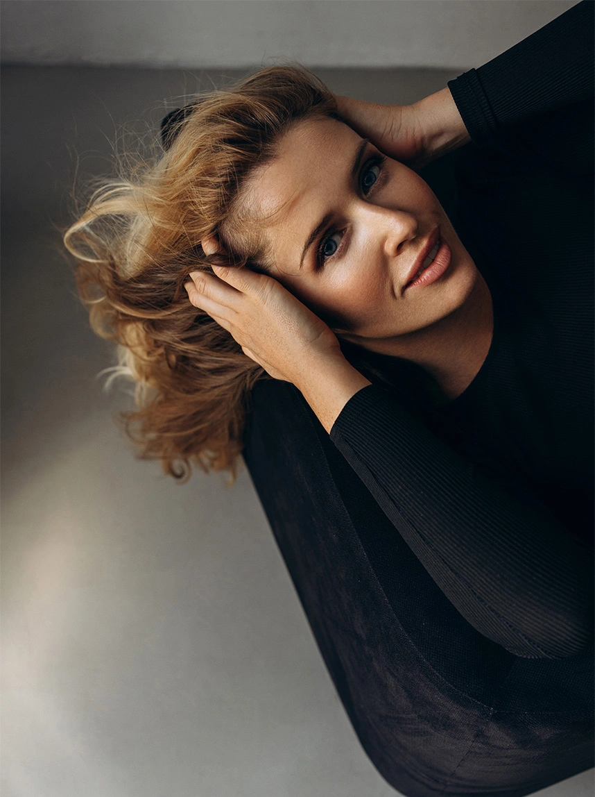 A woman with blonde hair wearing a black top leans back, looking directly at the camera. The image showcases her clear, healthy eyes and refreshed upper facial area. - Chalazion Incision Drainage in Arizona