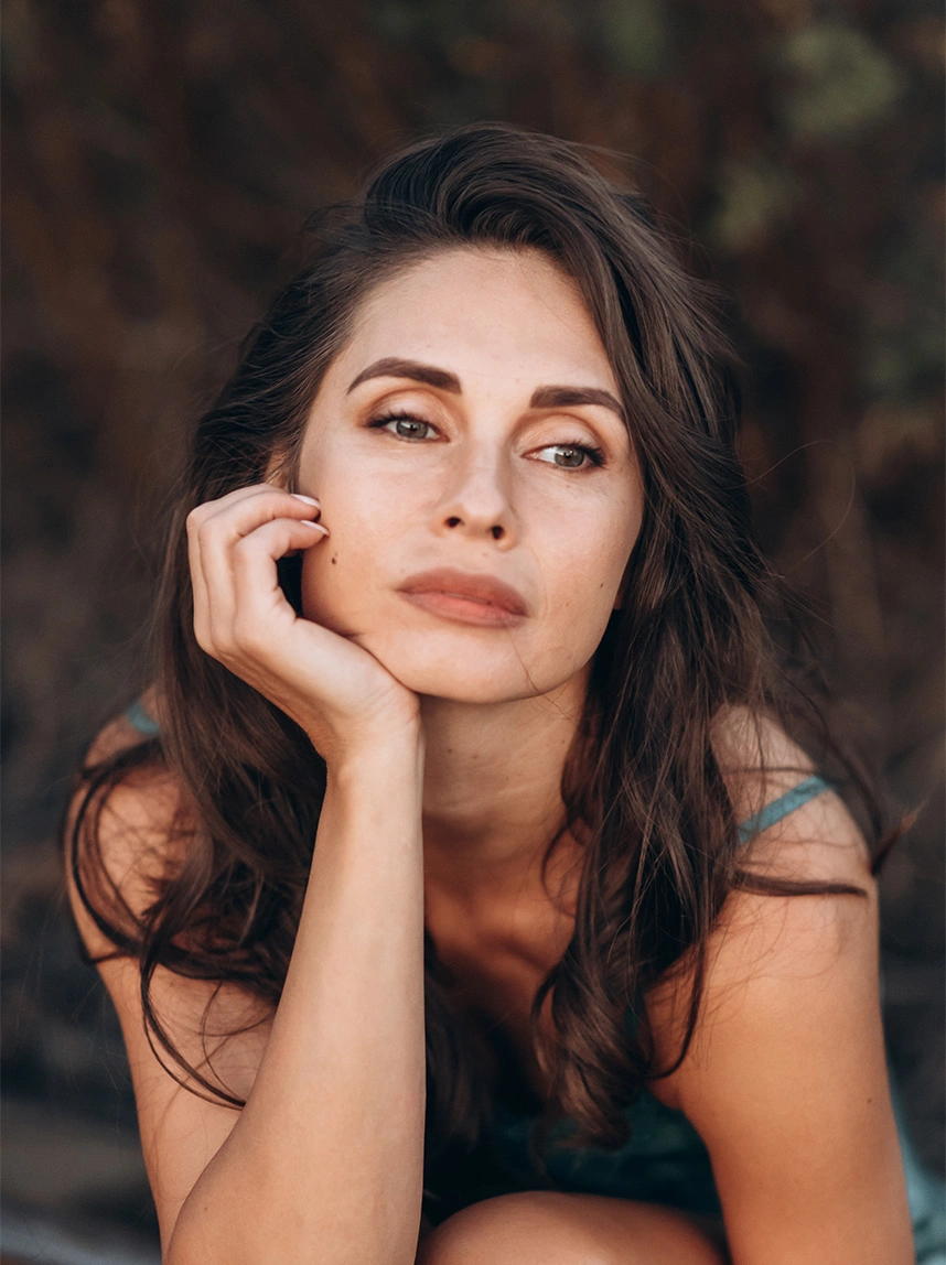 A close-up portrait of a woman with brunette hair resting her chin on her hand. The soft, natural lighting emphasizes her smooth, firm jawline and rejuvenated facial contours. - Deep Plane Facelift in Arizona