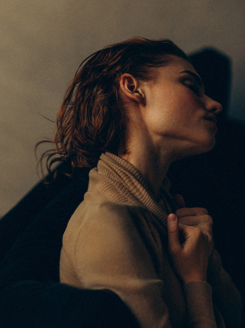 A profile shot of a woman with wet, reddish-brown hair tucked back, clearly showing the proportion and natural positioning of the ear against the head in a dramatic, low-light setting. - Ear Surgery Otoplasty in Arizona