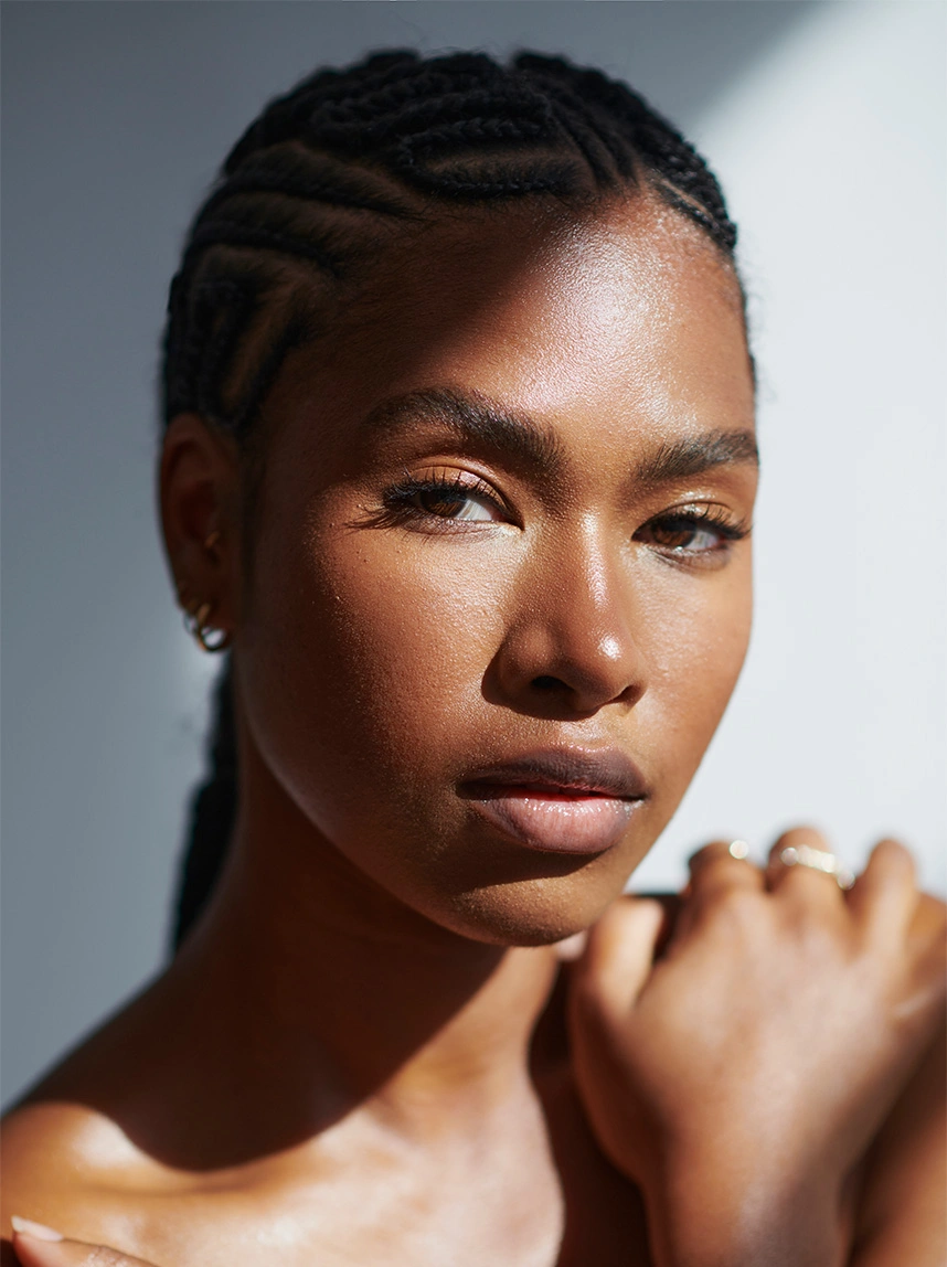 A close-up portrait of a woman with braided hair in soft, dramatic lighting, highlighting a balanced nasal bridge and refined facial symmetry. - Ethnic Rhinoplasty in Arizona