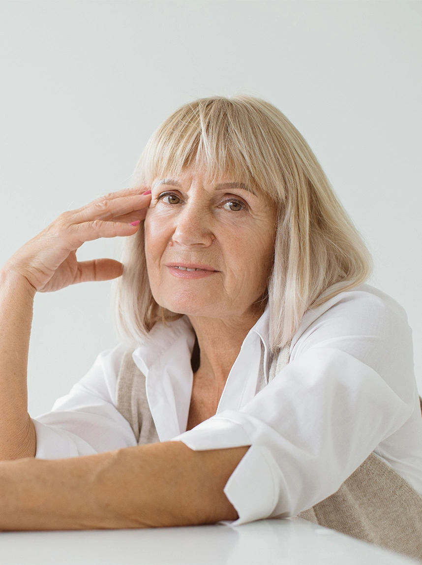 A portrait of an older woman with blonde hair and a white shirt, looking forward with a calm and natural gaze, emphasizing facial balance. - Eye Removal in Arizona