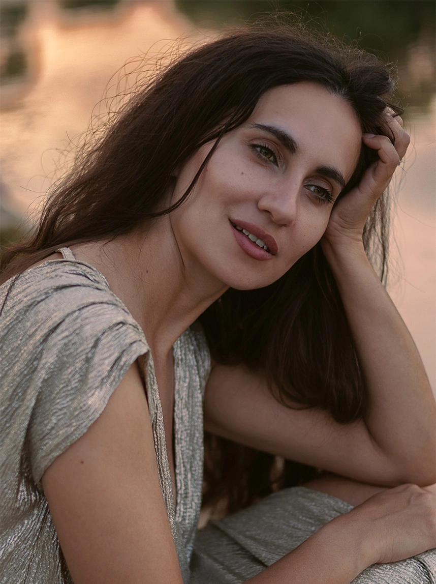 A woman with long dark hair in a shimmering silver dress smiles softly, highlighting a smooth, youthful upper eyelid area and rested appearance. - Eyelid Surgery in Arizona