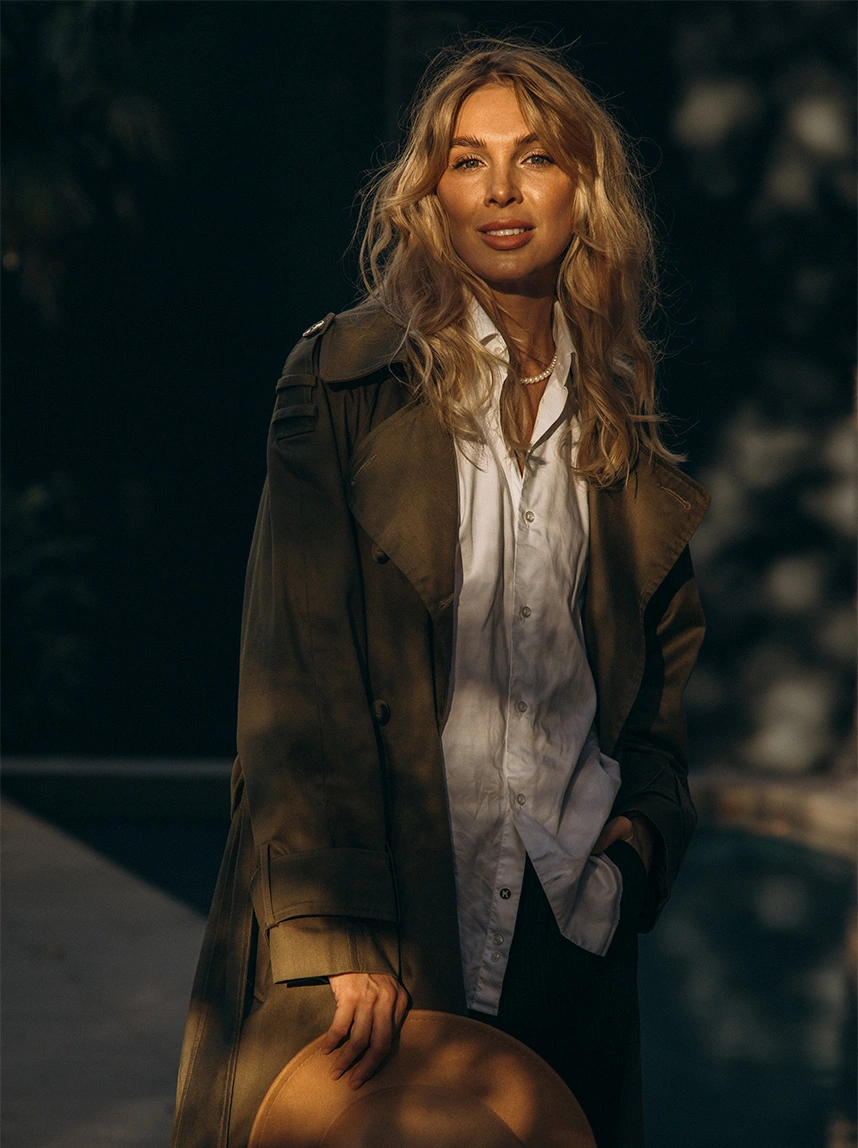 A woman with blonde wavy hair, wearing a white shirt and olive trench coat, displays a confident and symmetrical facial expression, representing restorative harmony. - Facial Nerve Paralysis in Arizona