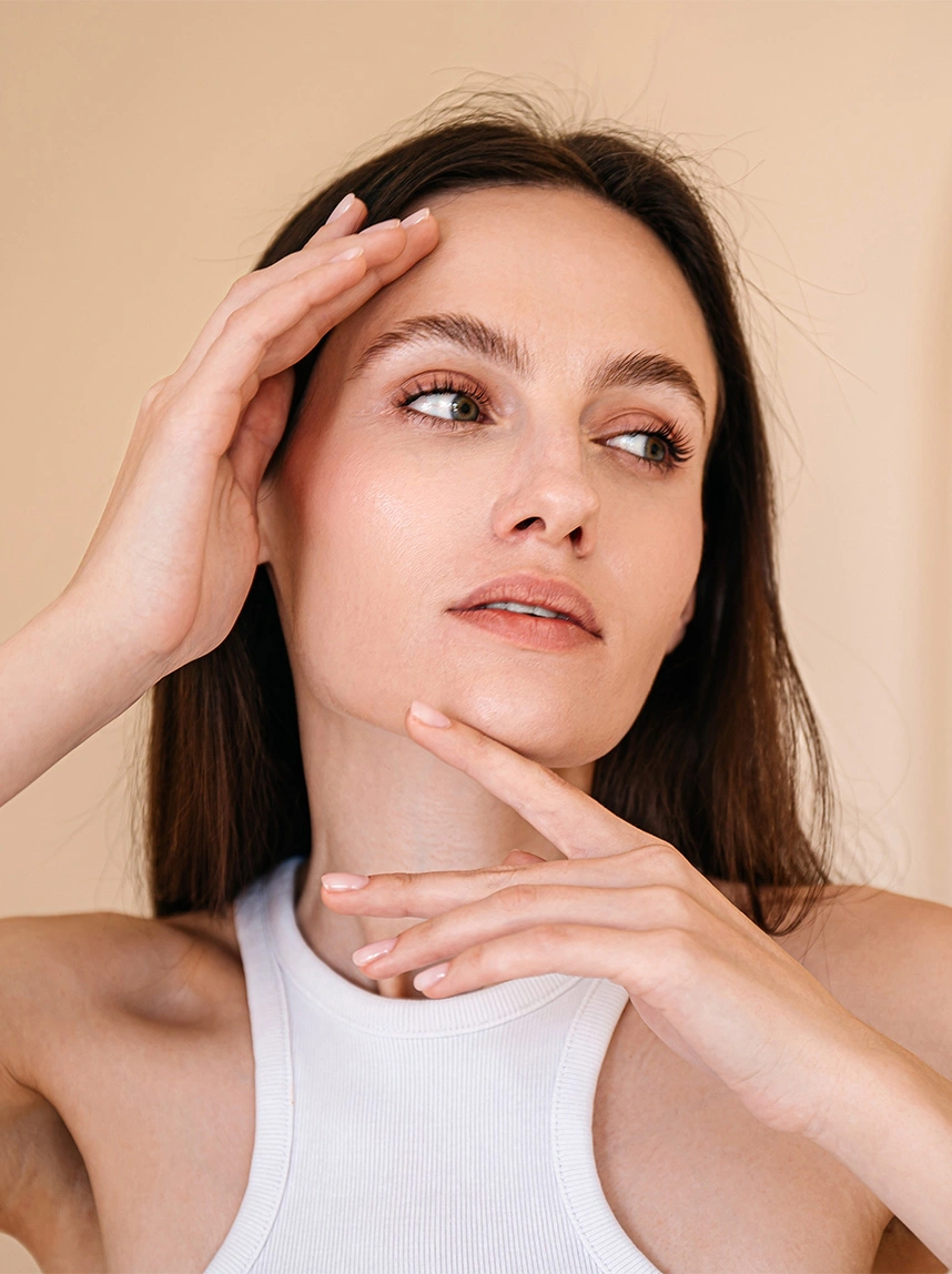A close-up portrait of a woman looking upward while touching her forehead and chin, featuring bright, alert eyes and clear, well-defined upper eyelid creases. - Functional Blepharoplasty in Arizona