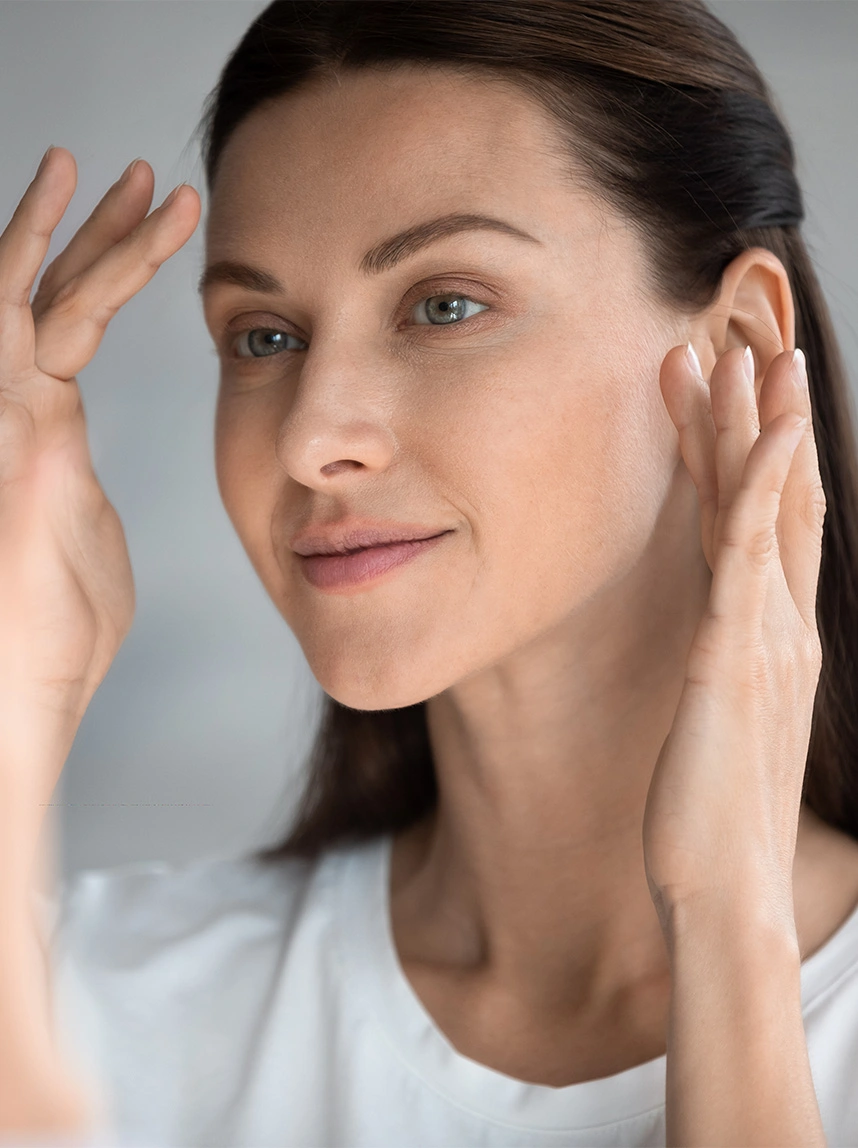 A close-up of a woman with her hair pulled back, touching her temples and forehead with a peaceful expression, representing relief and clarity. - Migranes in Arizona