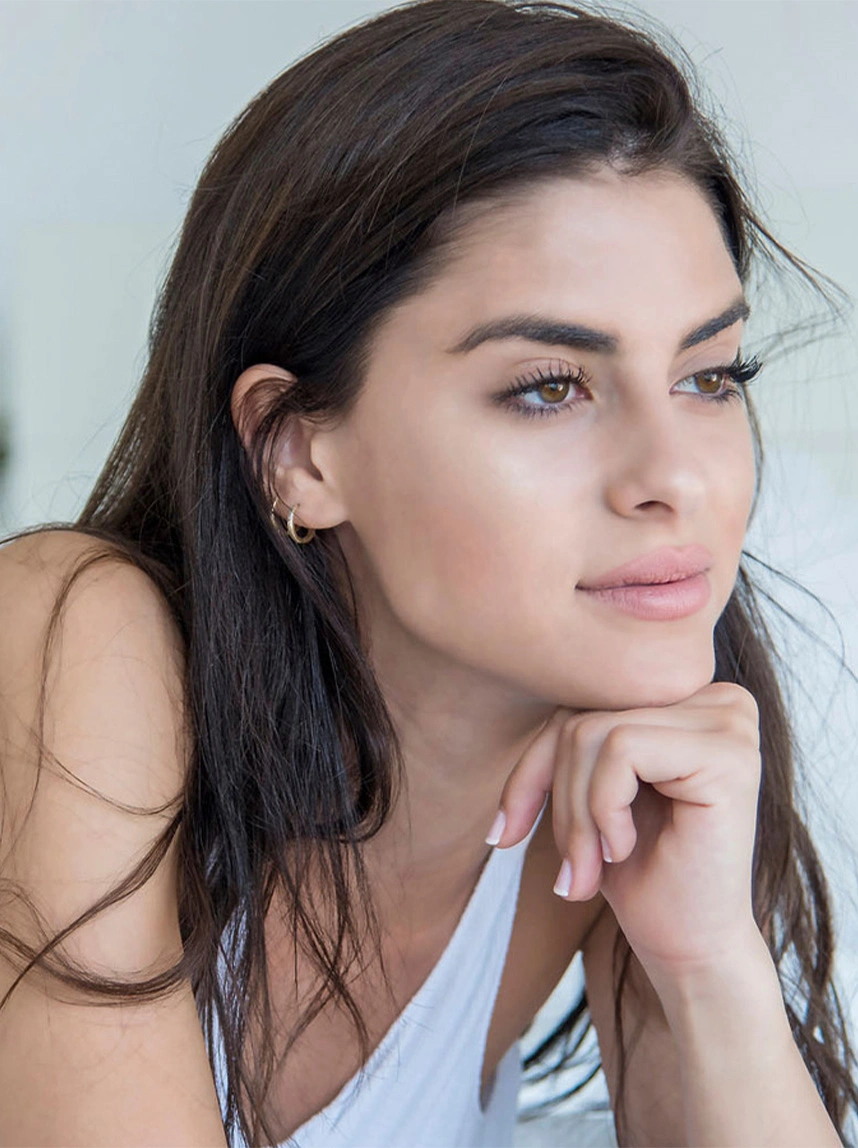 A portrait of a woman with long dark hair looking off-camera, showcasing a straight, balanced nasal bridge and harmonious facial profile. - Non-Surgical Nose Job in Arizona