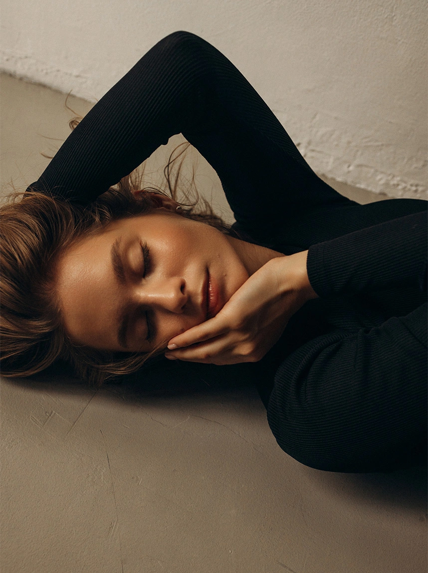 A woman in a black top lies down with her eyes closed, resting her face on her hand. Her radiant skin and peaceful expression represent vitality and internal health restoration. - Peptide Therapy in Arizona