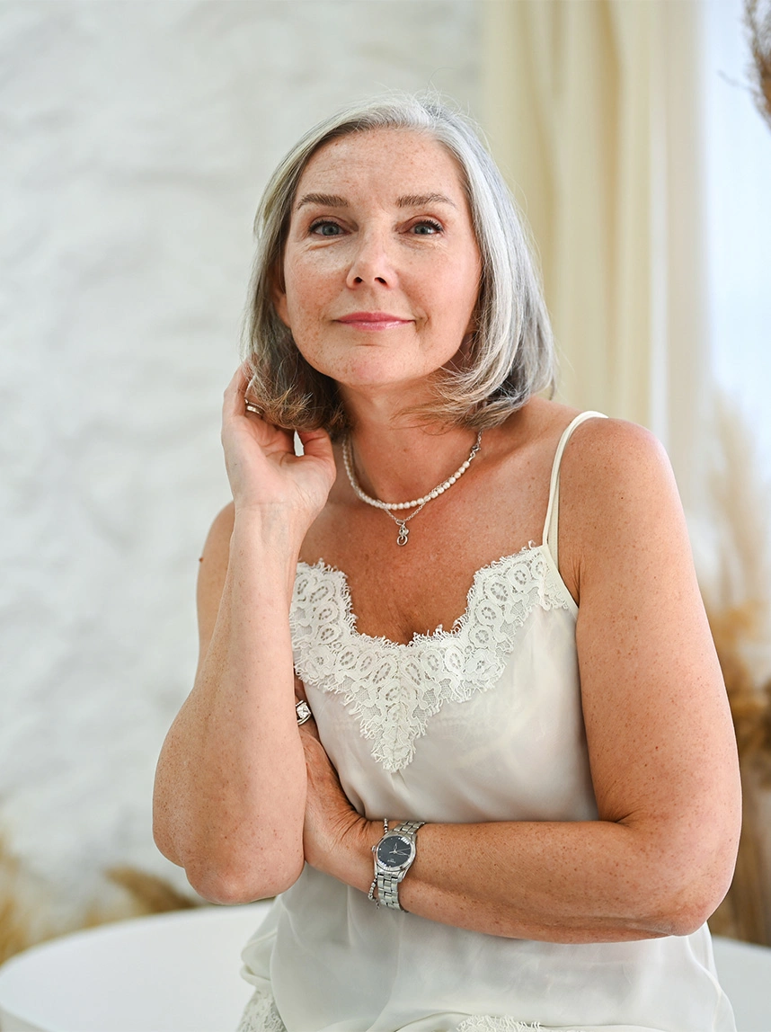 A portrait of a woman with silver hair, wearing a white lace-trimmed camisole and a pearl necklace. She looks directly at the camera with clear, well-rested eyes and a balanced facial expression. - Thyroid Eye Disease in Arizona