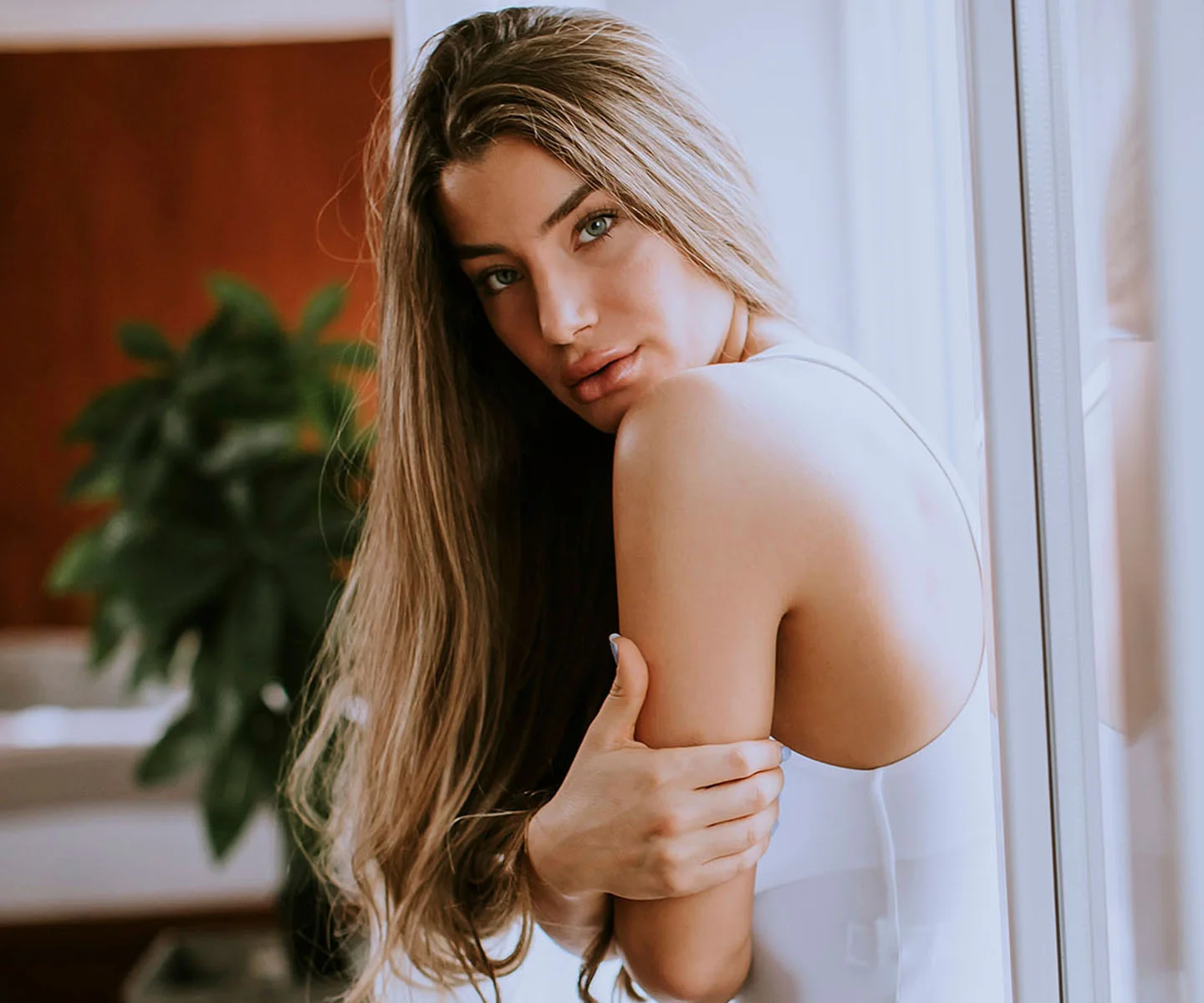 A bright and energetic lifestyle photograph of a person from the shoulders down, wearing a sleeveless white top. They are standing outdoors under bright sunlight, with their arms raised slightly. The background is a soft-focus blur of green foliage and a clear blue sky, evoking a feeling of confidence, freedom, and health. - Arm lift in Arizona