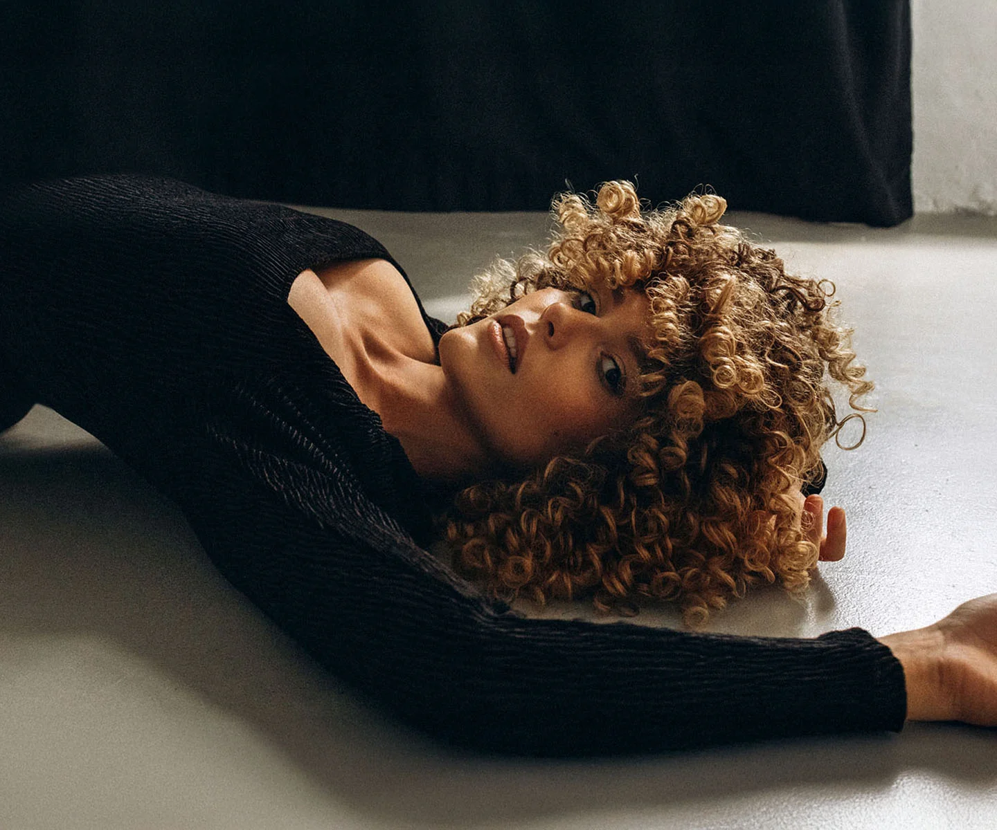 A bright, high-key lifestyle image of a woman with her back slightly turned toward the camera, looking over her shoulder with a bright, cheerful smile. She is wearing a simple white tank top. The background is a crisp, clean white, emphasizing a feeling of physical lightness, comfort, and newfound energy. - Breast reduction in Arizona