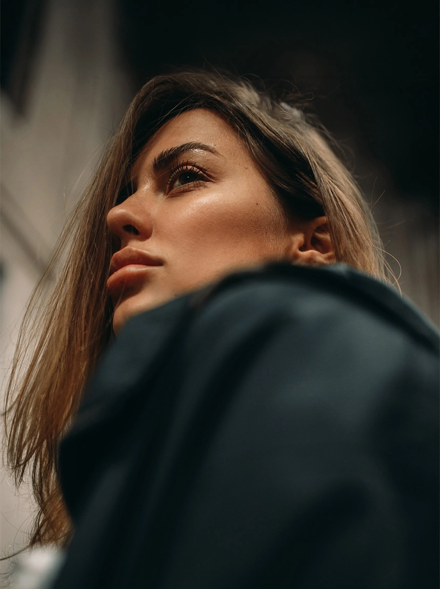 A low-angle profile shot of a woman looking upward, showcasing a smooth forehead and naturally elevated, well-defined eyebrows against a moody, dark background. - Brow Lift in Arizona