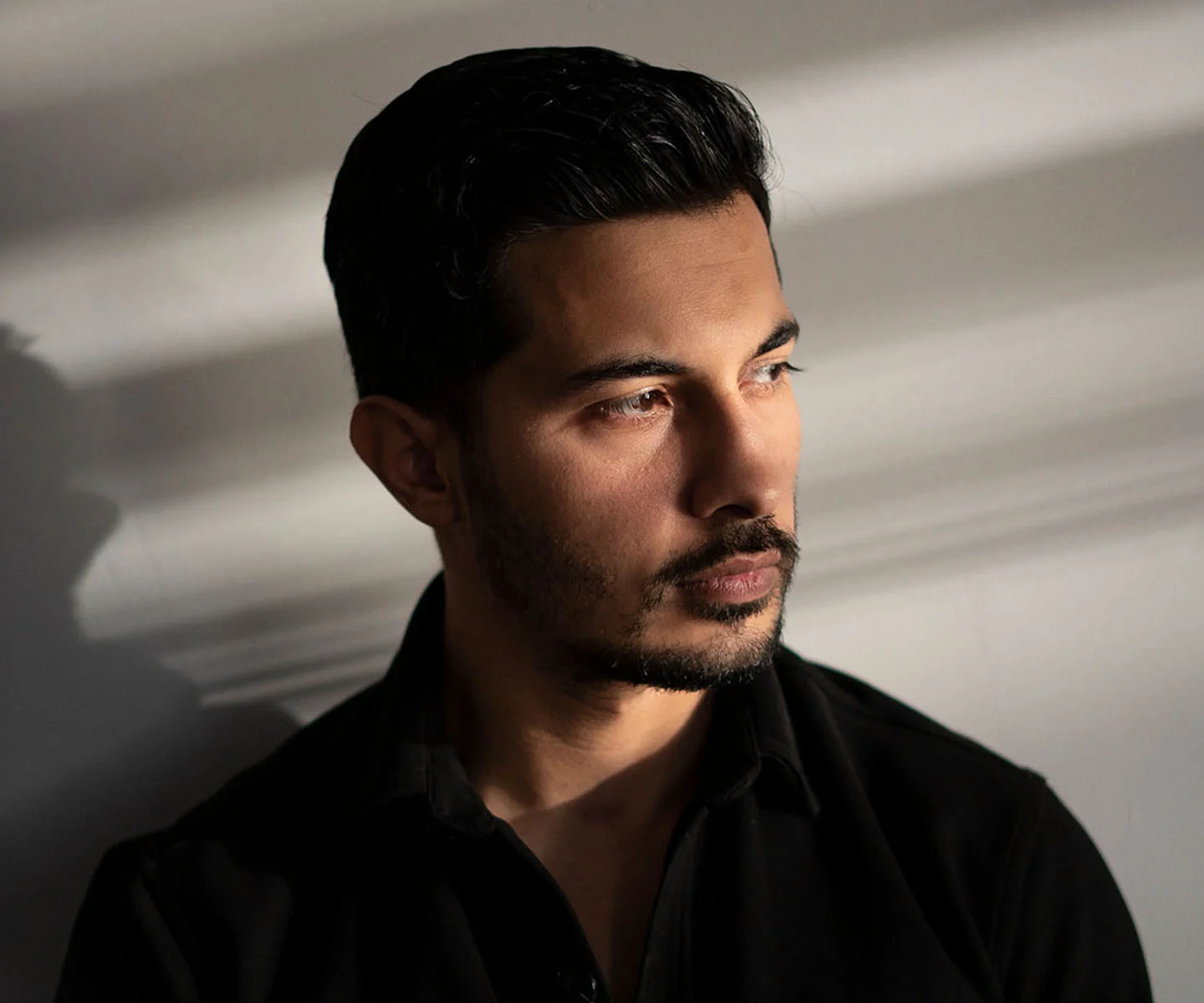 A profile shot of a woman with her hair pulled up into a loose bun, clearly revealing the ear and side of the head. She has a serene expression and is looking slightly upward. The background is a soft, warm neutral tone, and the side-lighting accentuates the natural shape and position of the ear in relation to the face. - Ear surgery in Arizona