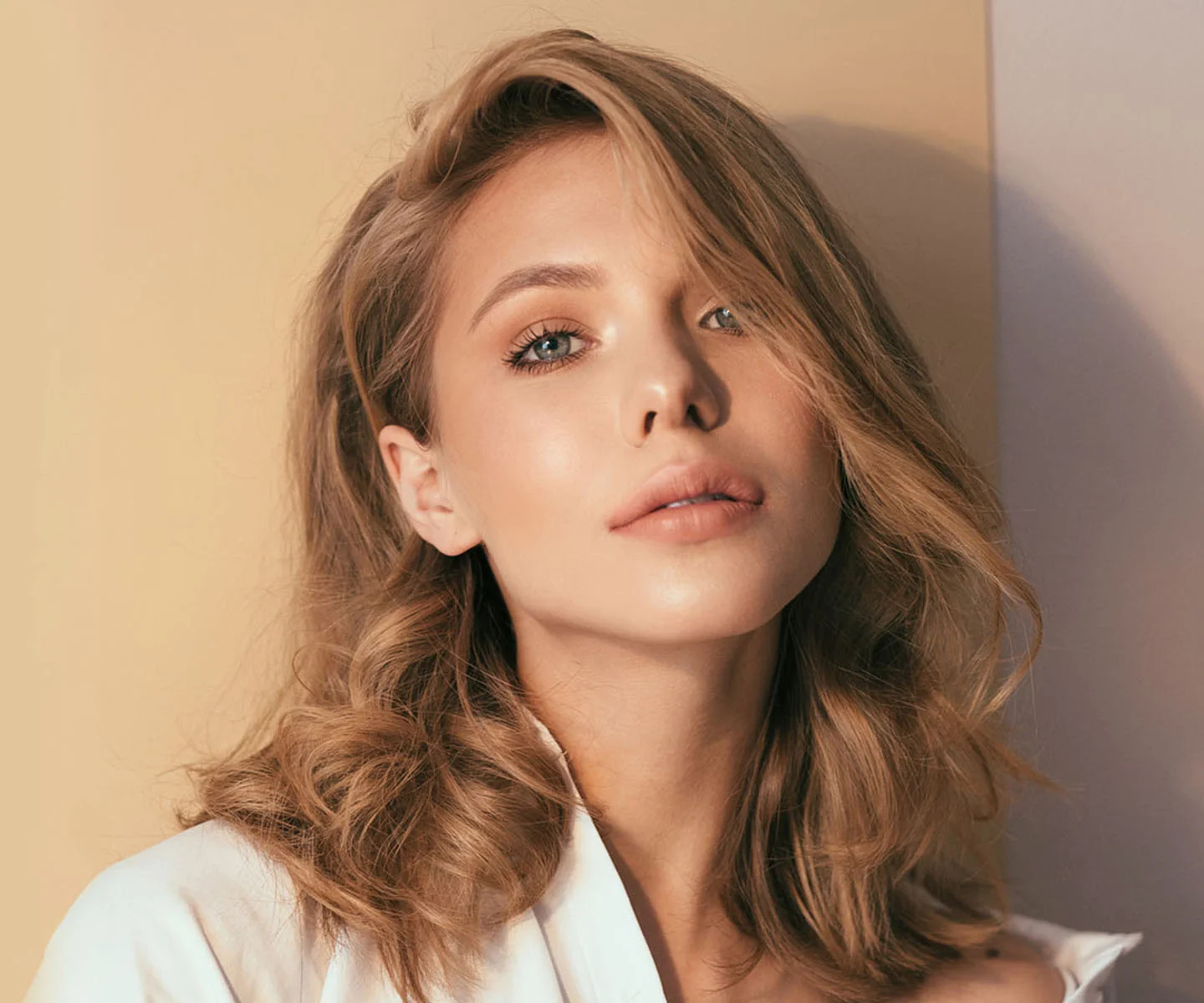 A portrait of a woman with blonde wavy hair and blue eyes looking into the camera. Soft, warm sunlight highlights her balanced facial features and smooth, rejuvenated skin texture. - Face & Eyelid Reconstruction in Arizona