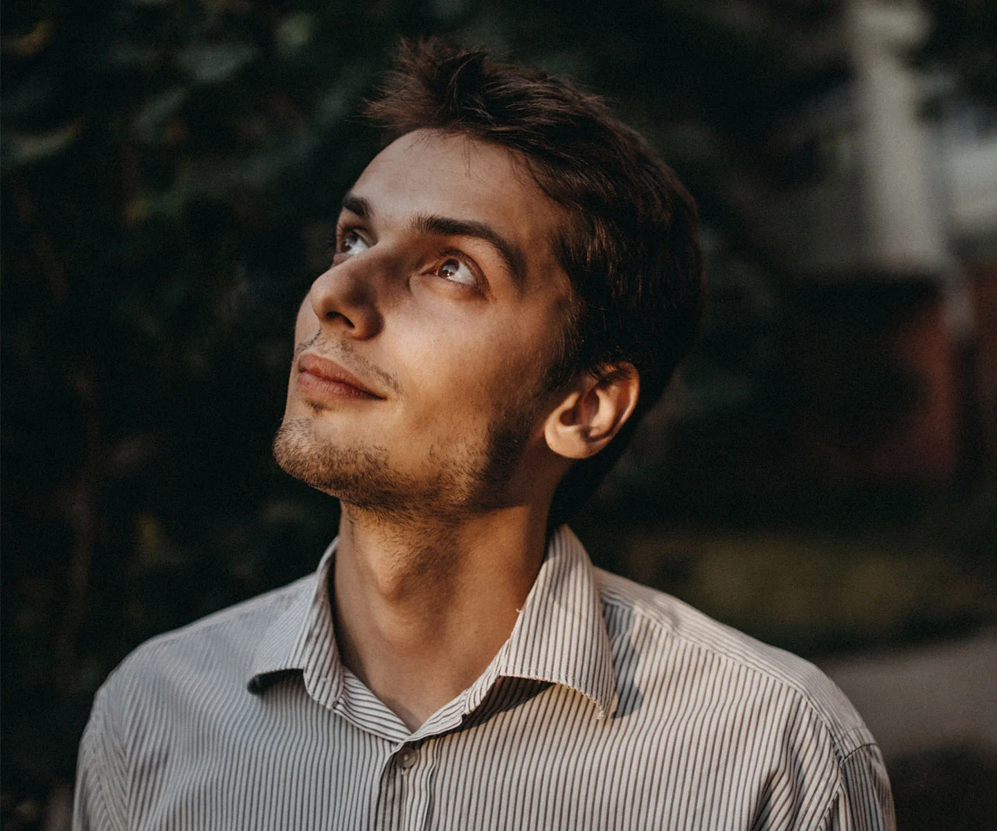 A man with short brown hair looks upward into the light, showcasing a full, natural-looking hairline and healthy hair density against a soft-focus outdoor background. - Hair Restoration in Arizona
