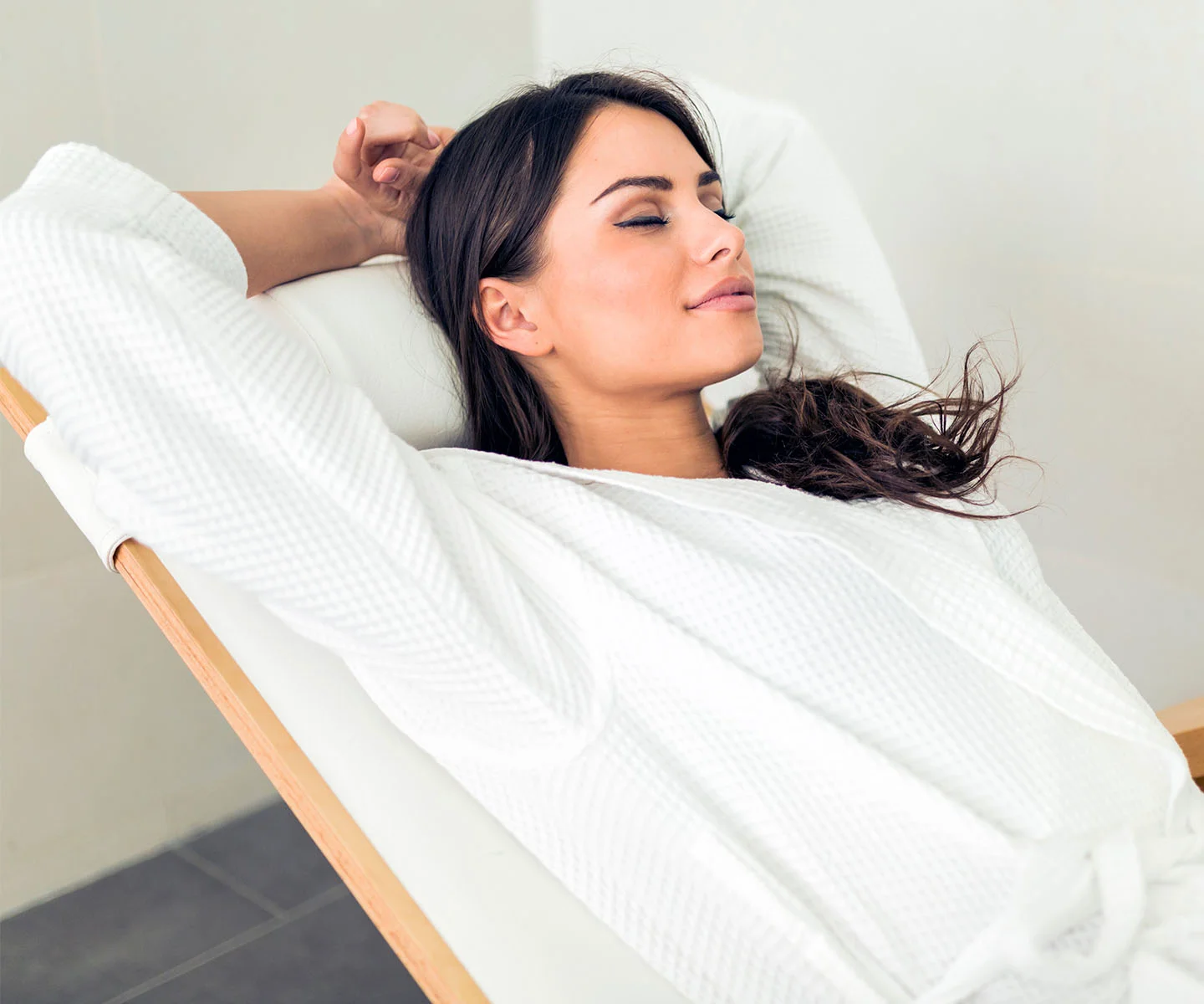 A woman in a white waffle-weave robe rests comfortably with her eyes closed and arms behind her head, illustrating a peaceful recovery process and a high-end wellness environment. - Hormone Oxygen Therapy in Arizona