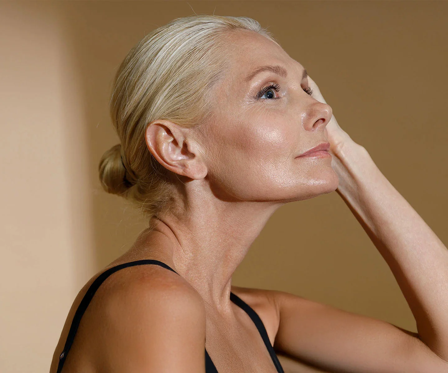 A side-profile portrait of a woman with blonde hair pulled into a bun. She looks upward with a serene, pain-free expression, showcasing smooth skin and a refreshed appearance. - Migrane Surgery in Arizona