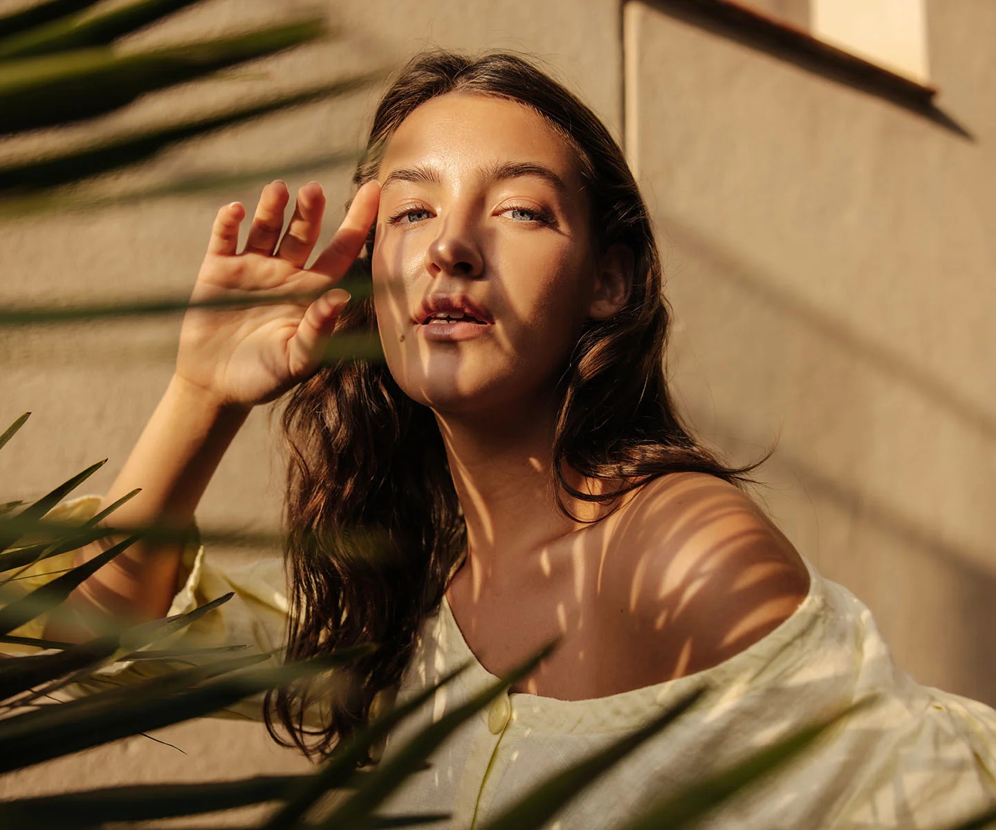 A portrait of a woman looking upward into the sunlight, with patterns of shadows from palm leaves falling across her face, showcasing clear, healthy eyes and comfortable, aligned eyelashes. - Misaligned Eyelashes in Arizona