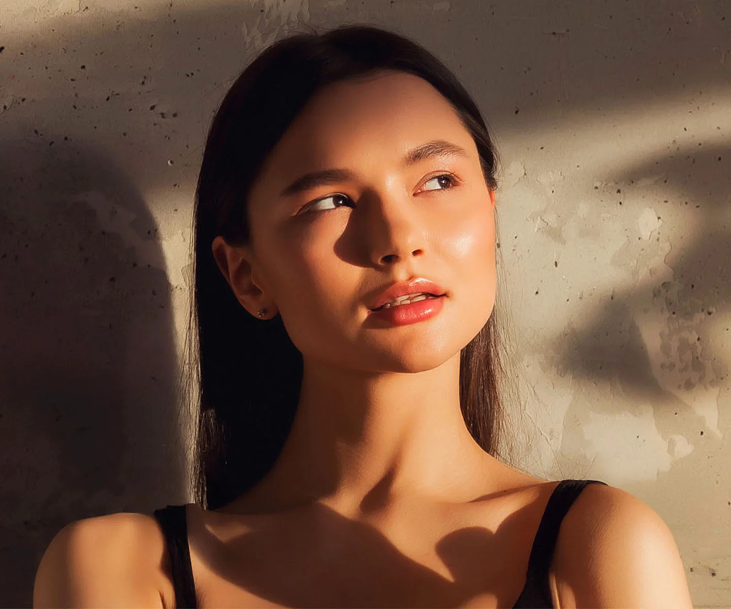 A woman with a glowing, radiant complexion looks off to the side as warm, golden sunlight falls across her face, highlighting the even tone and healthy texture of her skin. - Red Light Therapy in Arizona