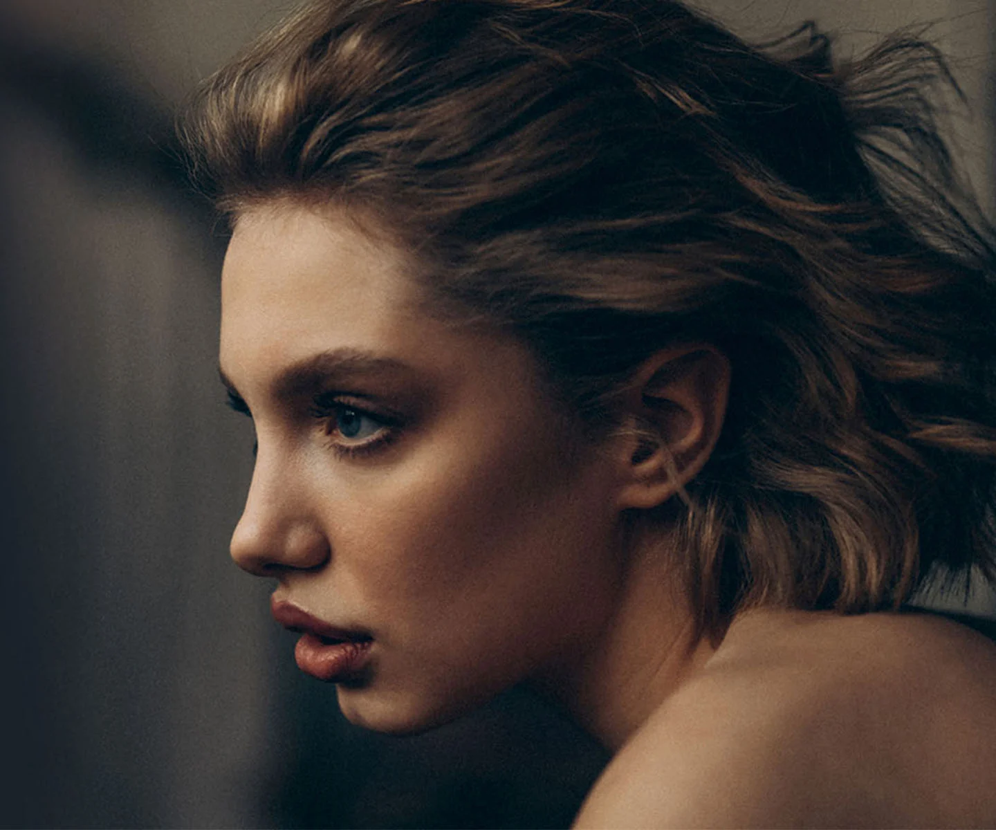 A close-up profile view of a woman with striking blue eyes and wavy hair, emphasizing the natural-looking, symmetrical bridge and tip of her nose in soft, dramatic lighting. - Revision Rhinoplasty in Arizona