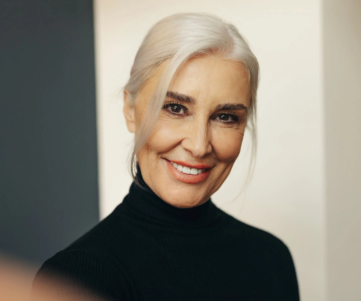 A portrait of a smiling woman with silver-white hair wearing a black turtleneck. Her bright, alert eyes and symmetrical expression showcase a rested and rejuvenated appearance. - Thyroid Eye Diesease in Arizona