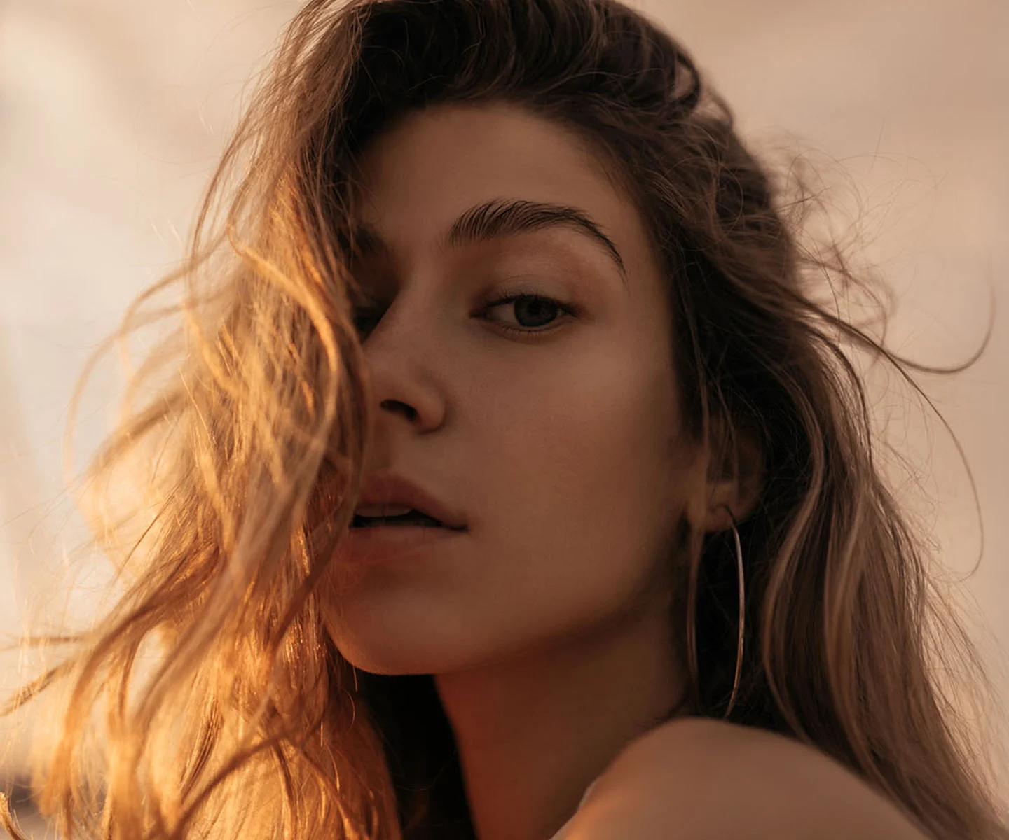 A close-up, warm-toned portrait of a woman with wavy hair. The soft lighting emphasizes smooth skin texture and clear, bright eyes. - Transcutaneous or Transconjunctival with CO2 Laser in Arizona